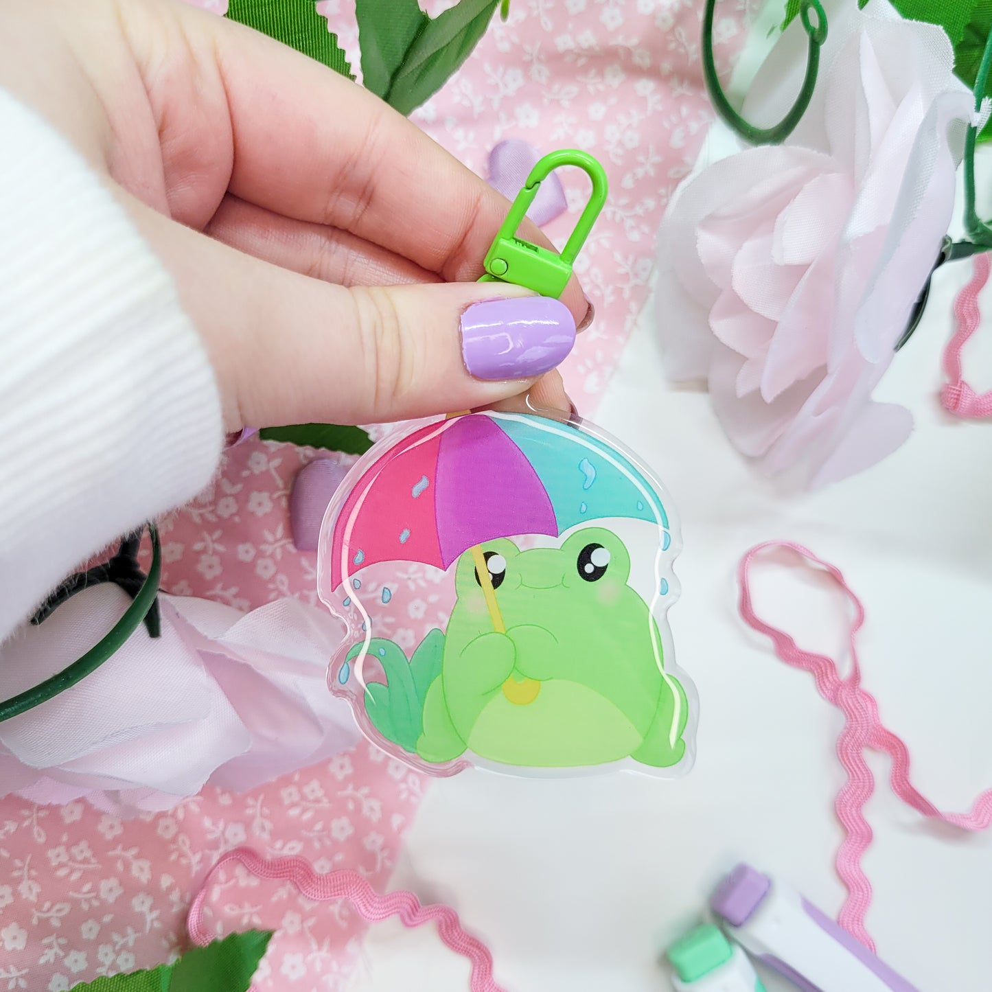 Cute Frog with an umbrella in the rain on an acryllic keychain, features a green clasp and double sided design with epoxy on the front