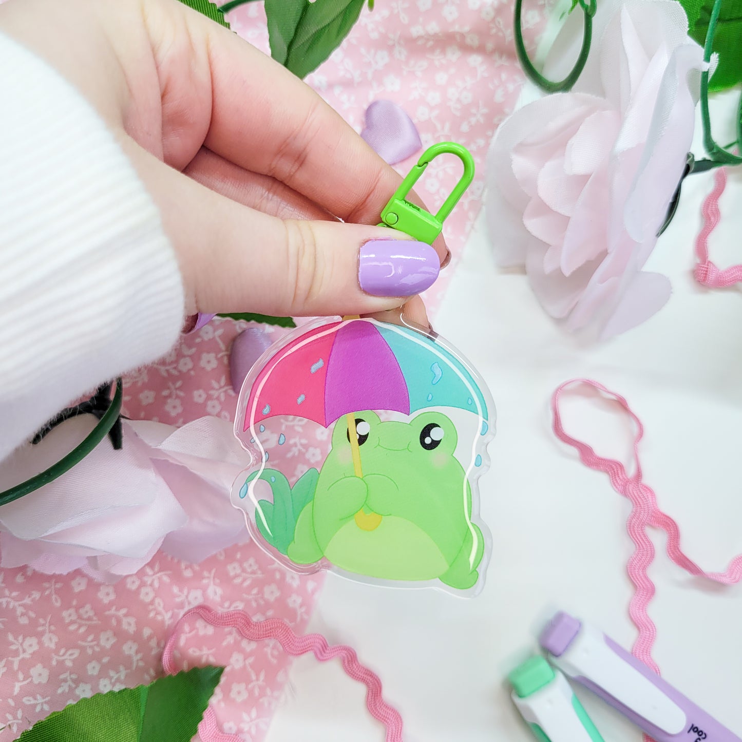 Cute Frog with an umbrella in the rain on an acryllic keychain, features a green clasp and double sided design with epoxy on the front