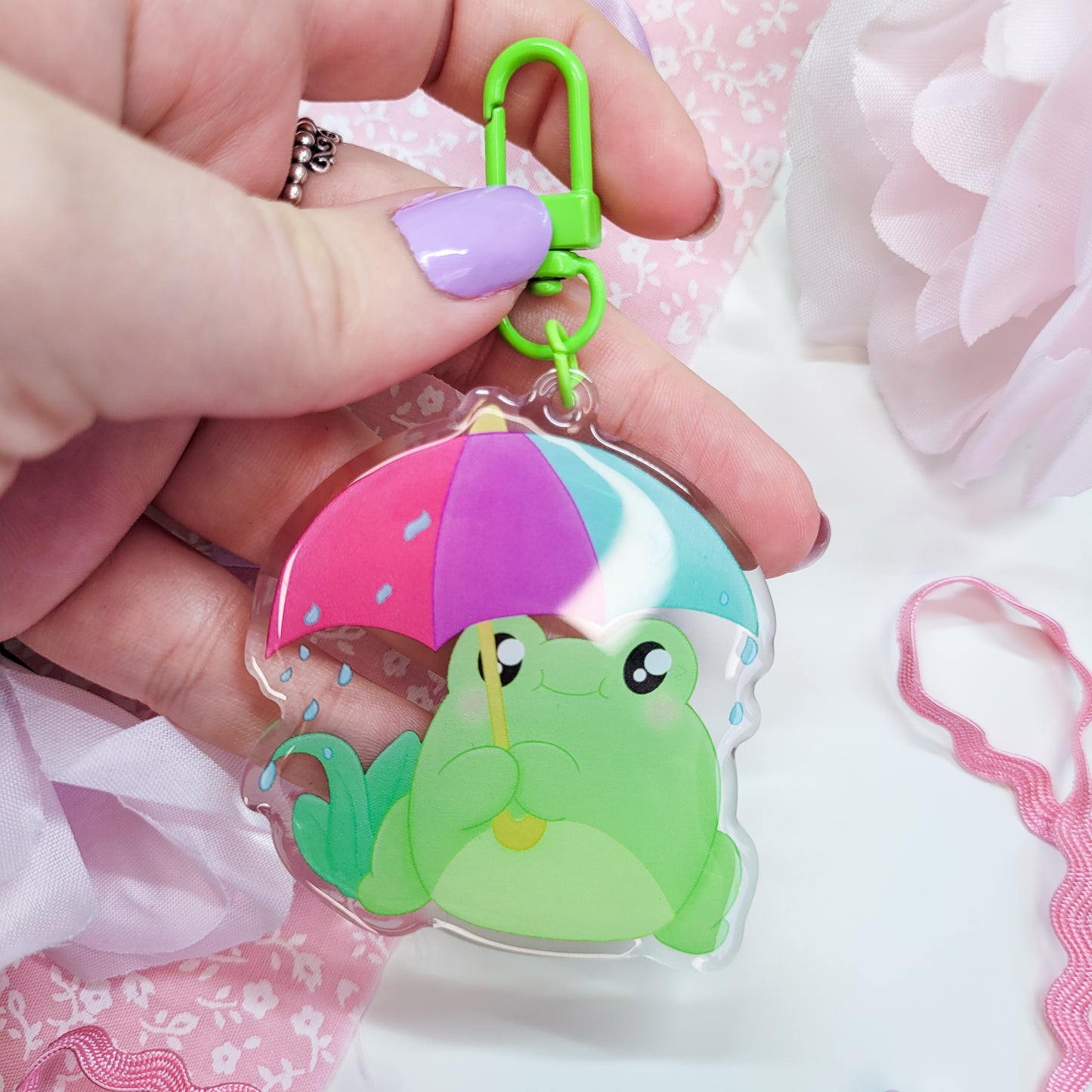 Cute Frog with an umbrella in the rain on an acryllic keychain, features a green clasp and double sided design with epoxy on the front