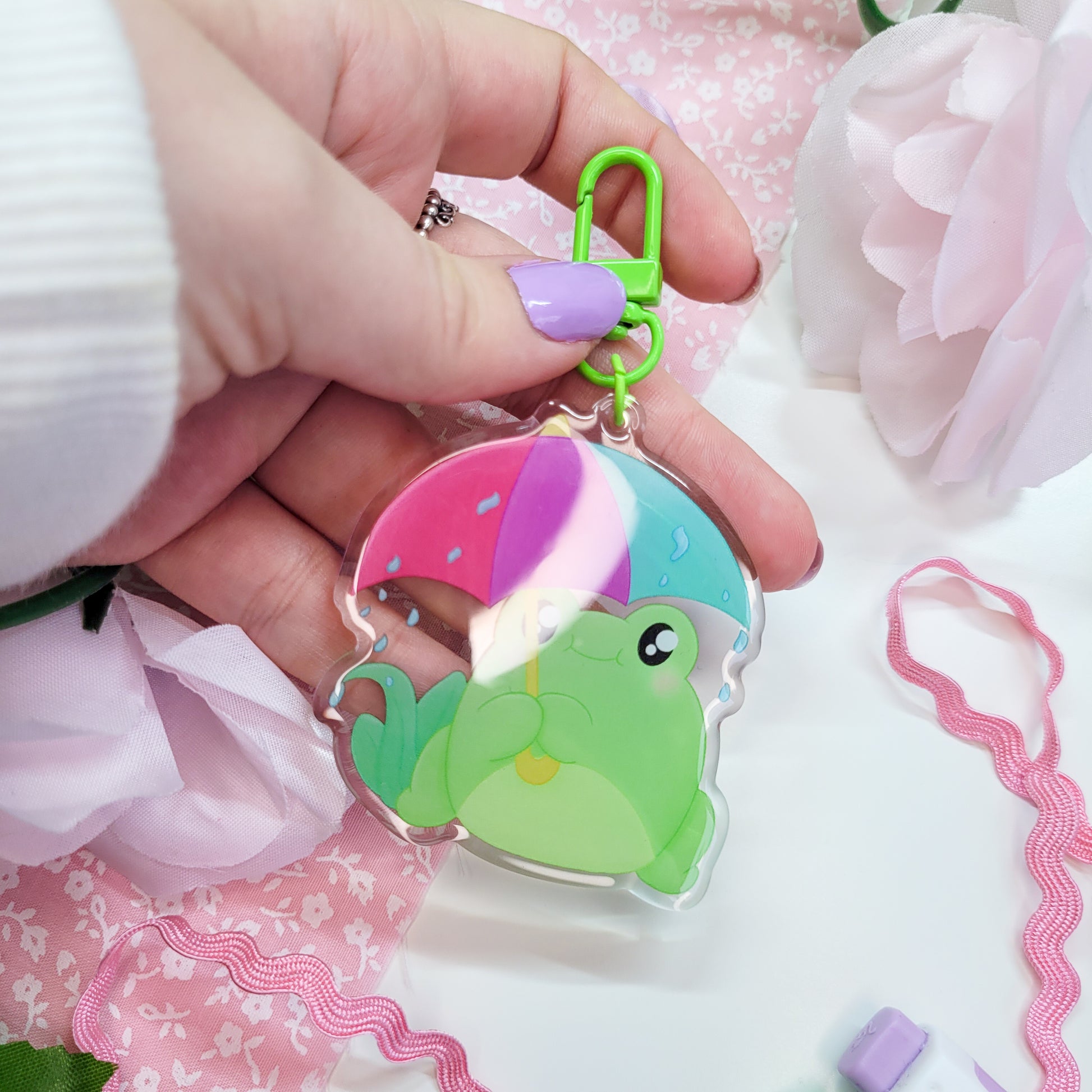 Cute Frog with an umbrella in the rain on an acryllic keychain, features a green clasp and double sided design with epoxy on the front