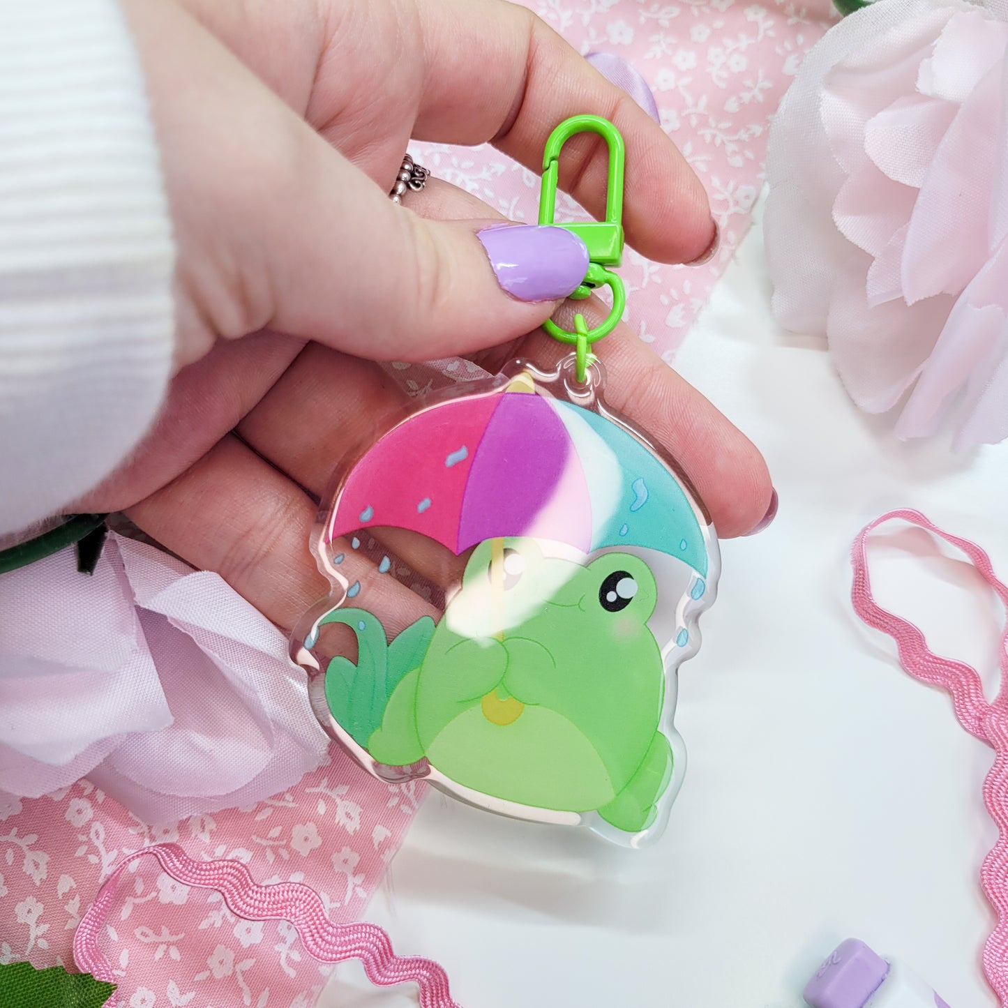 Cute Frog with an umbrella in the rain on an acryllic keychain, features a green clasp and double sided design with epoxy on the front