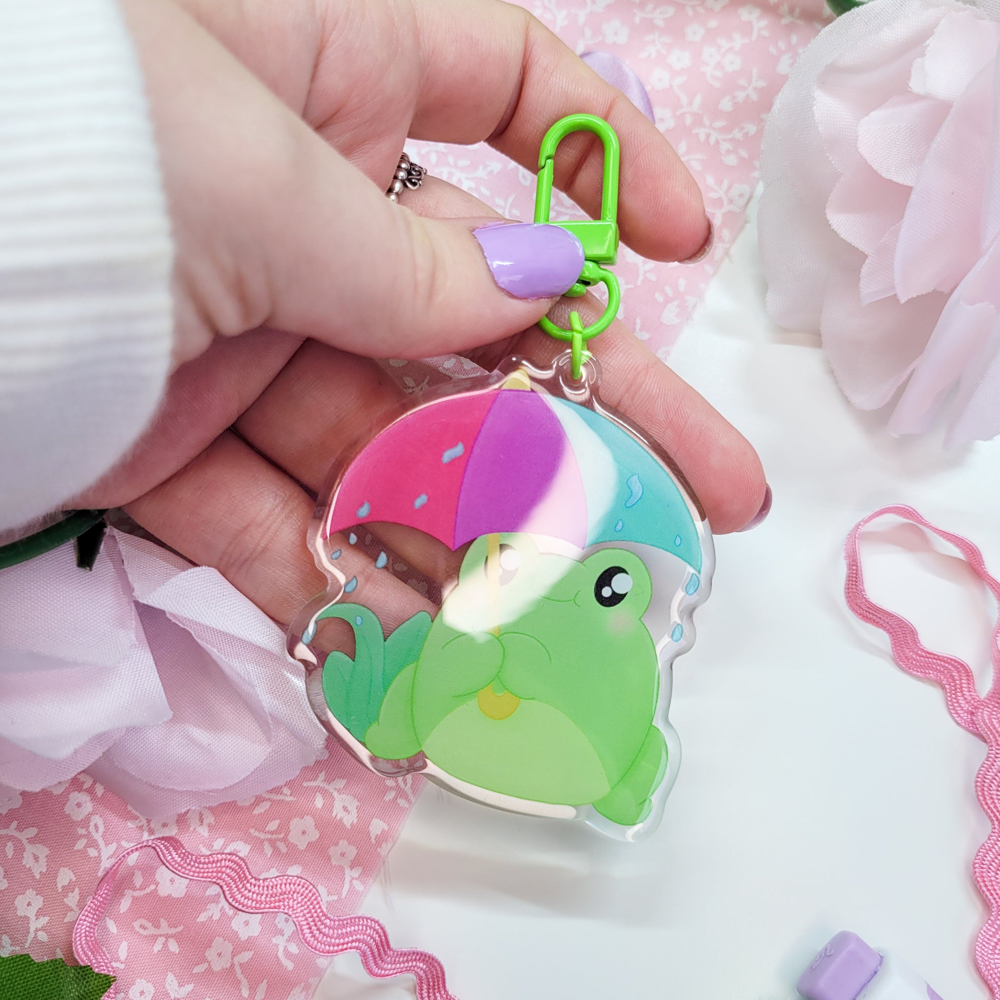 Cute Frog with an umbrella in the rain on an acryllic keychain, features a green clasp and double sided design with epoxy on the front
