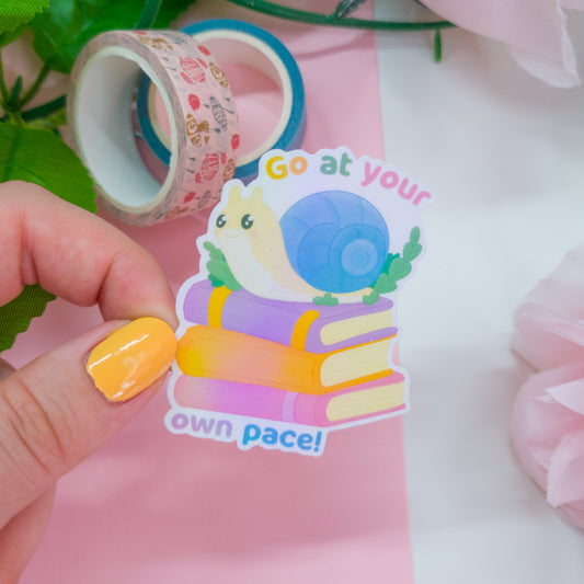 cute bookish sticker, featuring a cute snail on a stack of books and the text 'go at your own pace'