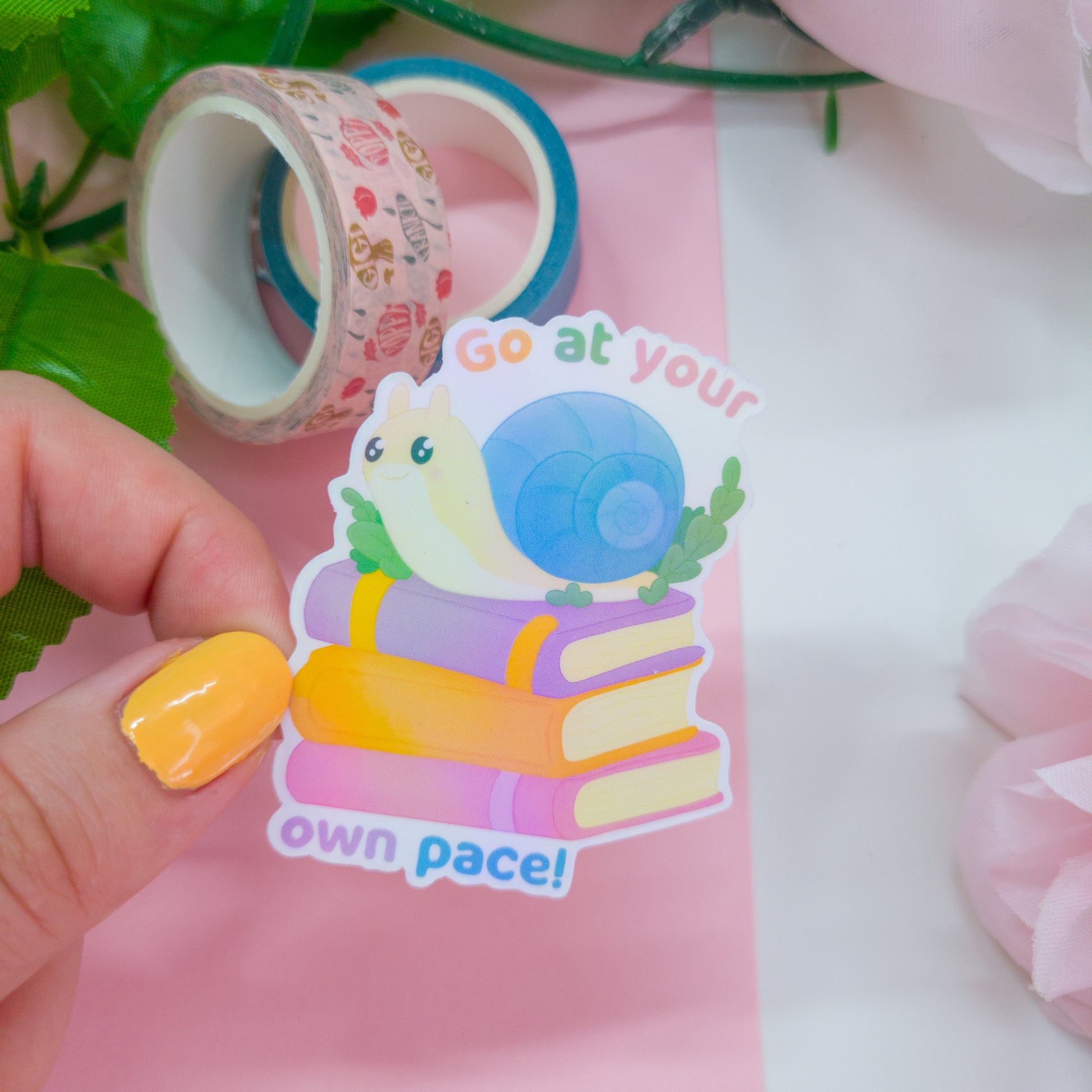 cute bookish sticker, featuring a cute snail on a stack of books and the text 'go at your own pace'
