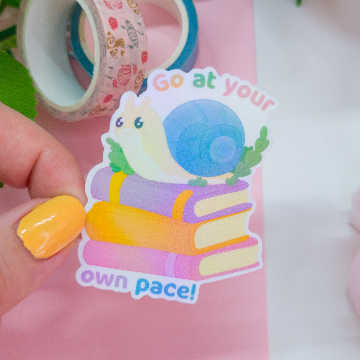 cute bookish sticker, featuring a cute snail on a stack of books and the text 'go at your own pace'