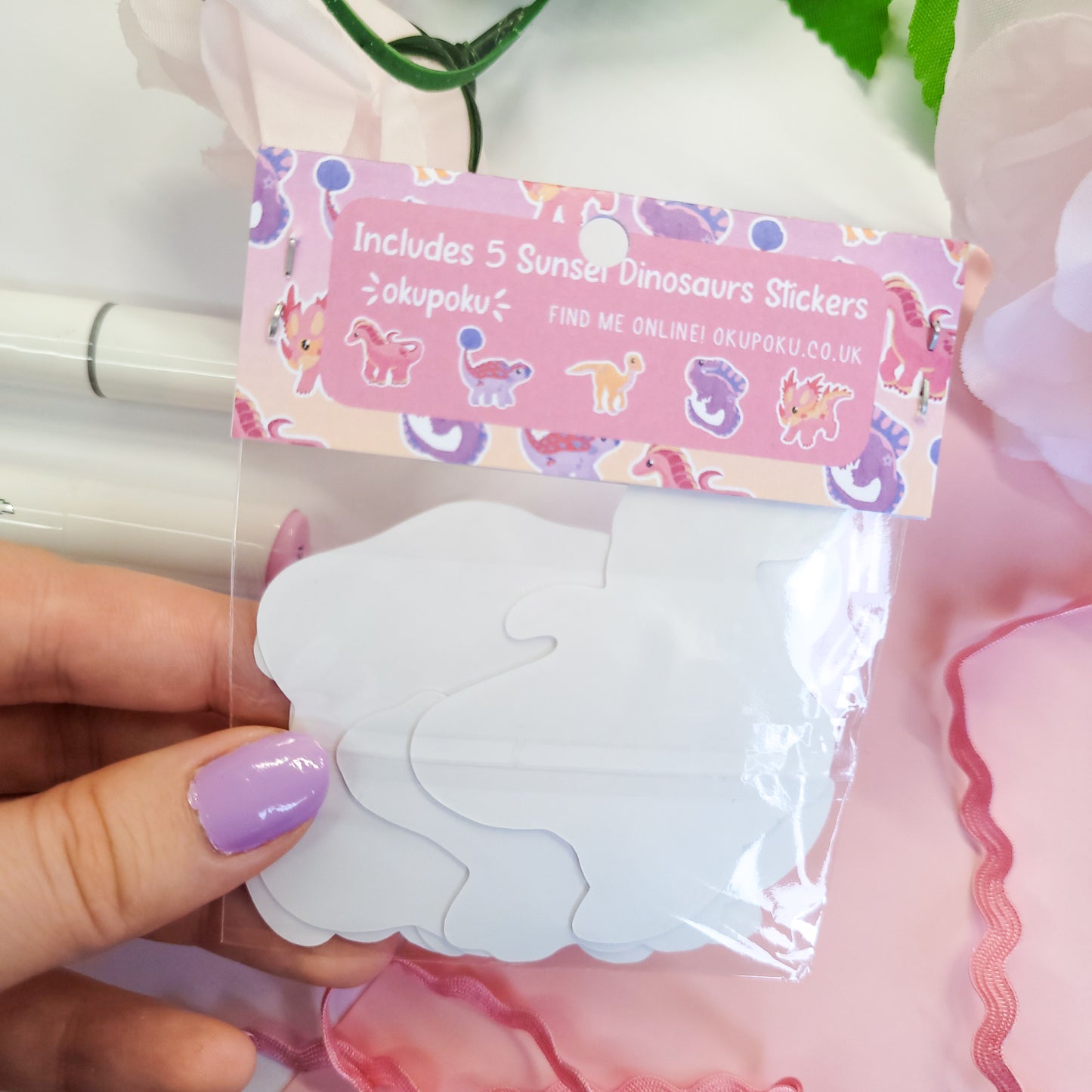 Packaged stickers with a pink label held by a hand against a floral background
