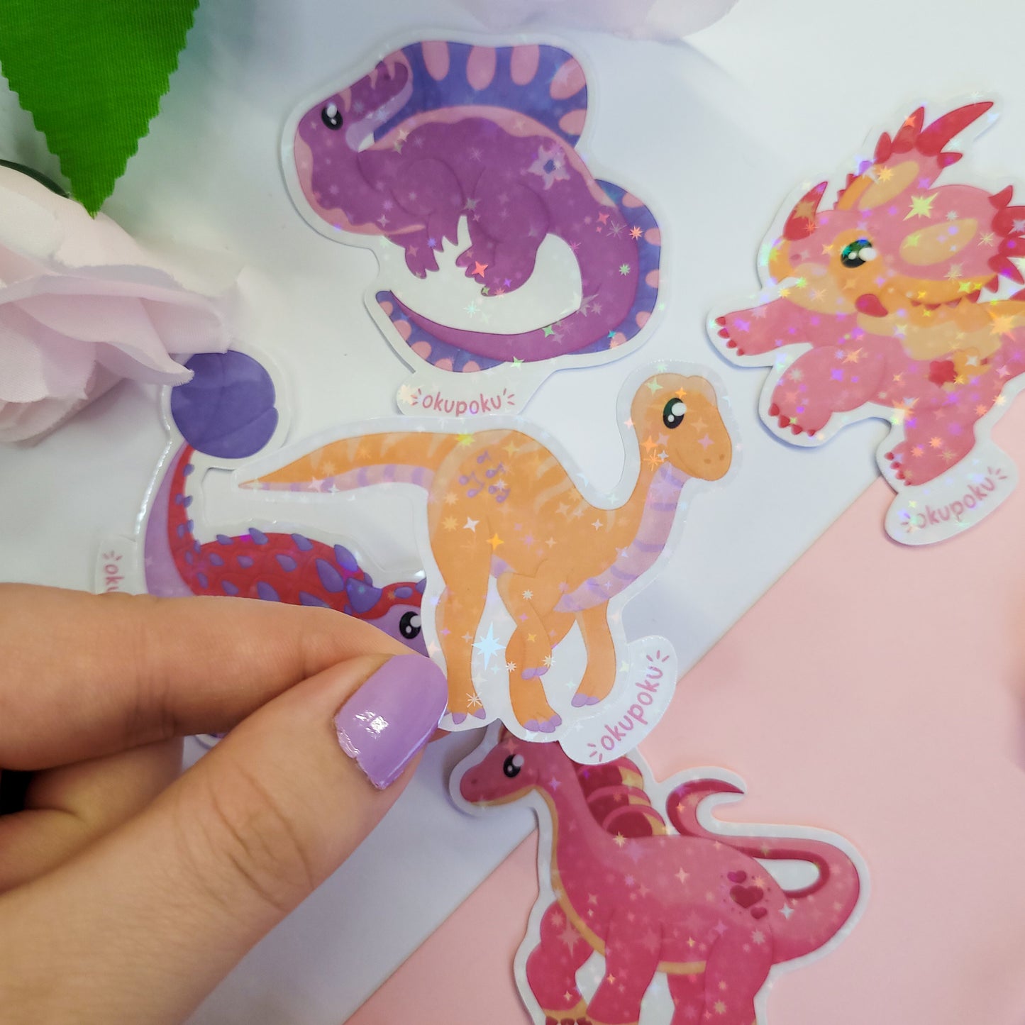 Colorful Gallimimus dinosaur stickers on a white background with a hand holding one of them.