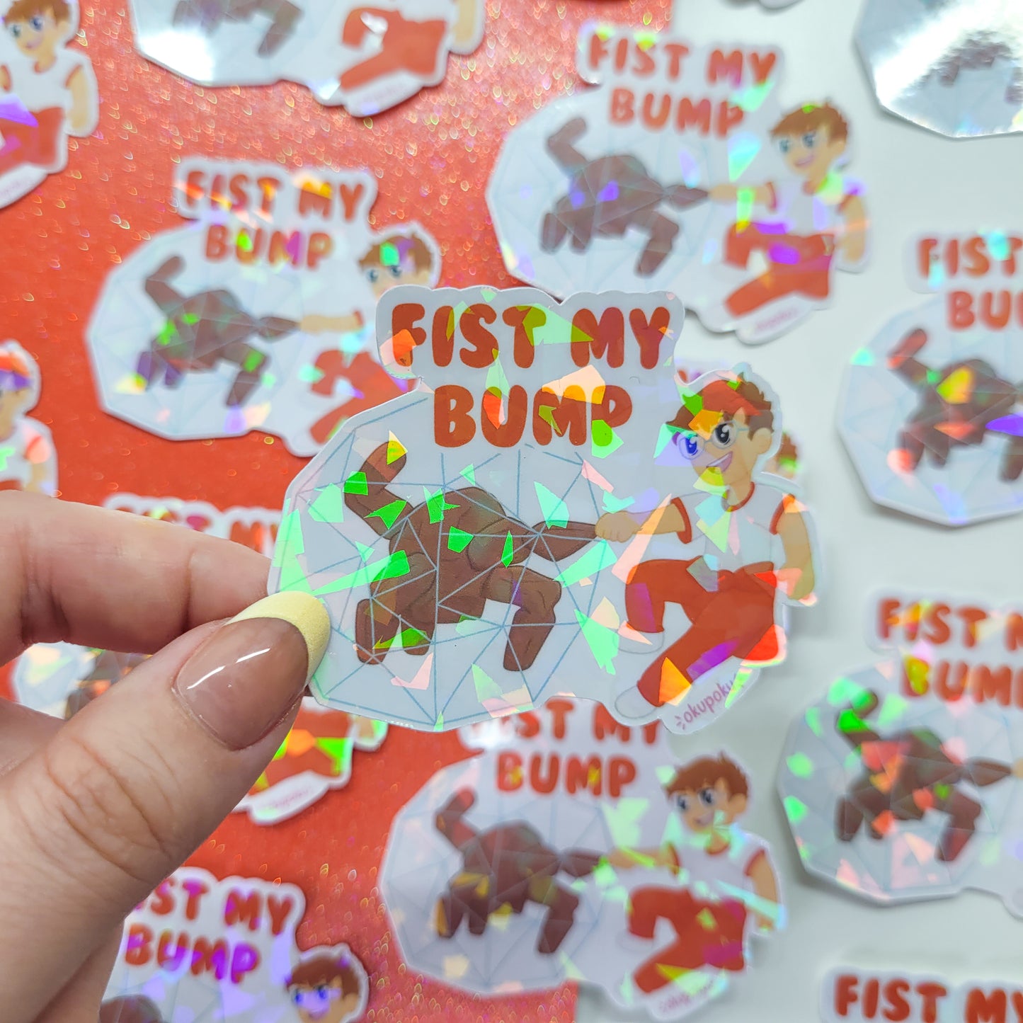 Holographic sticker with 'FIST MY BUMP' text held by a hand, with more stickers in the background.